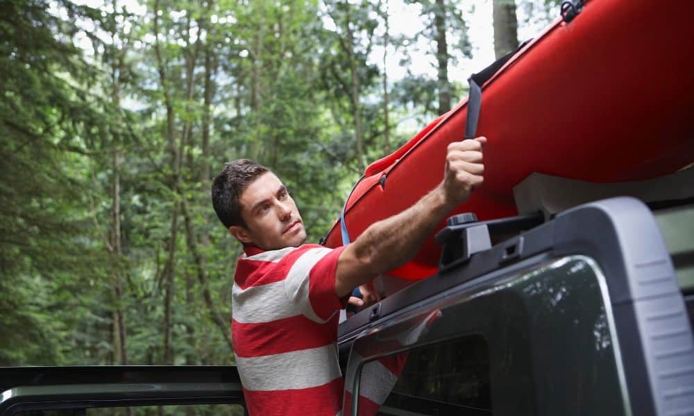 man tying kayak to car roof